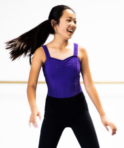 Jazz dancer wearing a leotard and leggings with her hair in a secured pony tail.